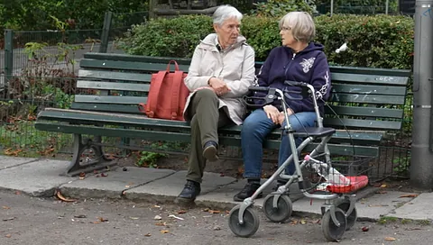 Zwei Seniorinnen auf einer Parkbank sitzend im Gespräch, mit Rollator