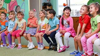 Lachende Kita-Kinder auf einer Bank sitzend