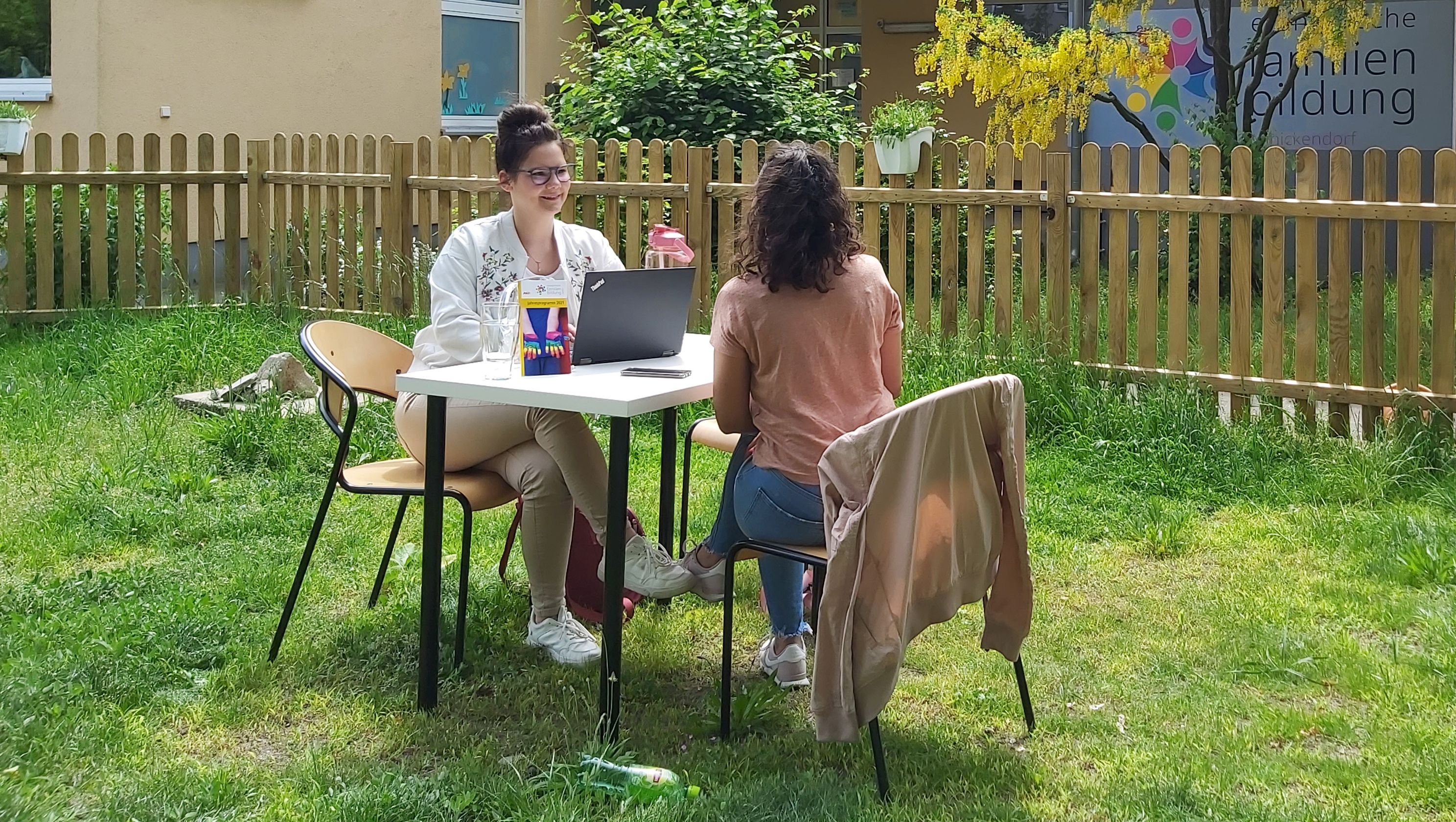 Zwei Frauen sitzen sich an einem Tisch im Garten gegenüber und sprechen miteinander