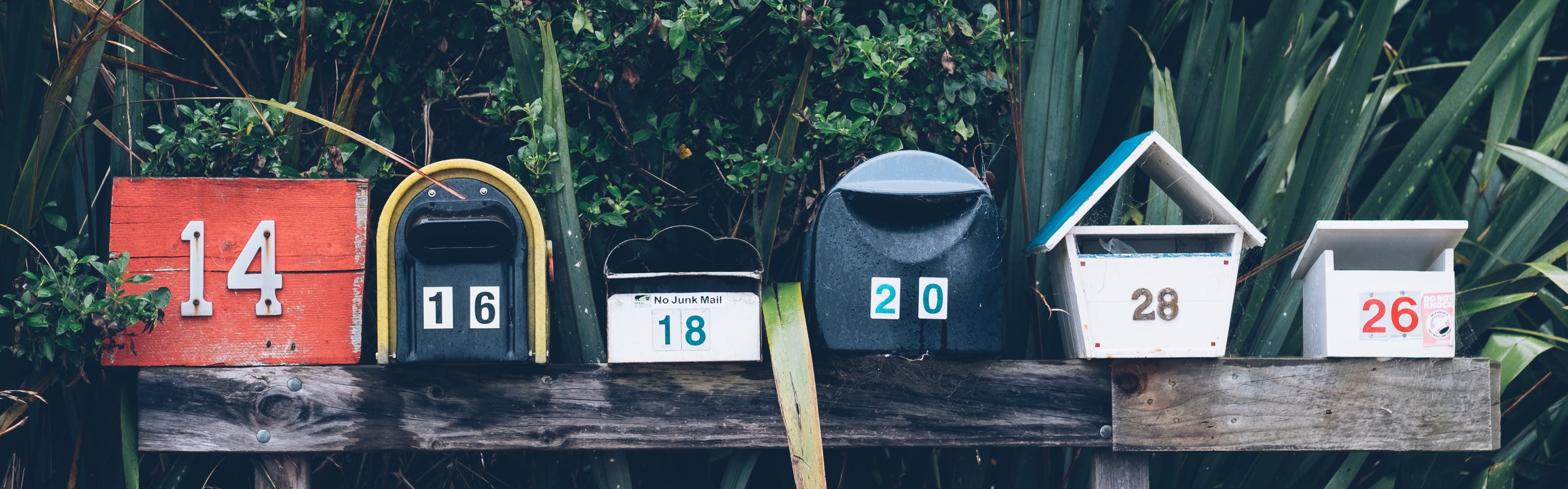 Unterschiedliche Briefkästen auf einem Holzbalken aufgereiht