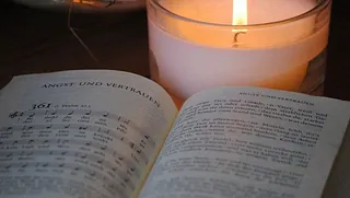 Aufgeschlagenes Gesangbuch mit brennender Kerze im Glas